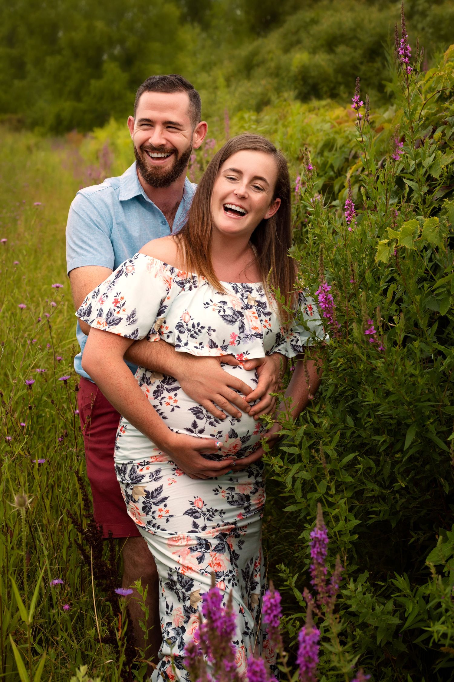 Maternity photos in a wildflower field with purple blooms and natural lighting.