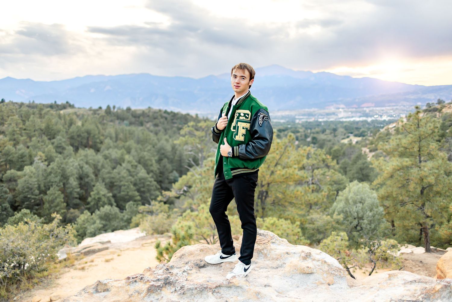 Senior guy stands on the rocks in letter jacket at his senior session at Palmer Park in Colorado Springs.
