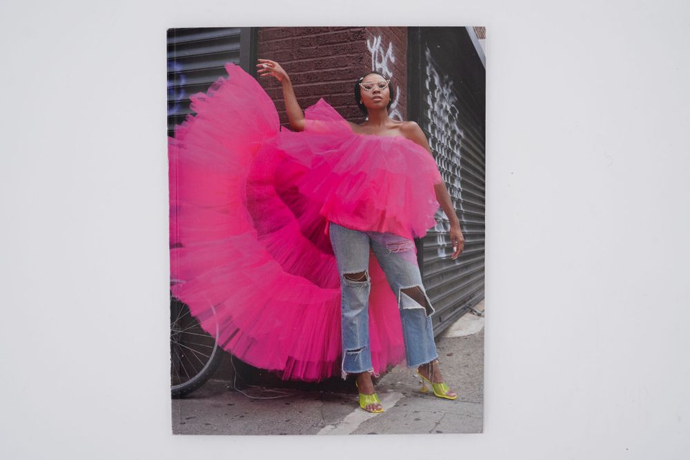 Person wearing dramatic hot pink tulle dress and yellow shoes poses against urban backdrop.