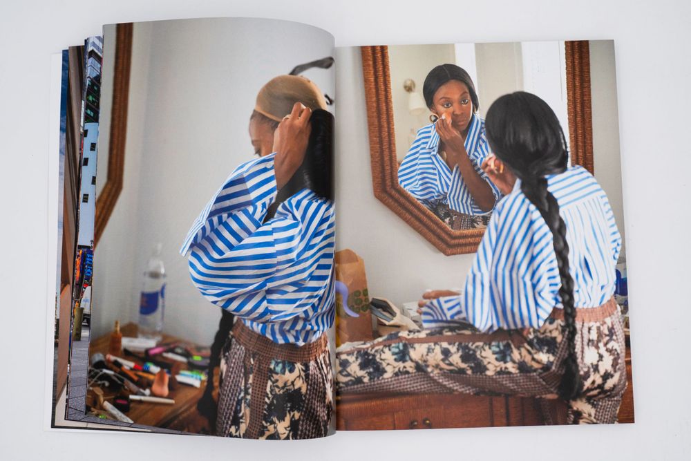 Magazine spread showing person in striped shirt applying makeup at vanity mirror.