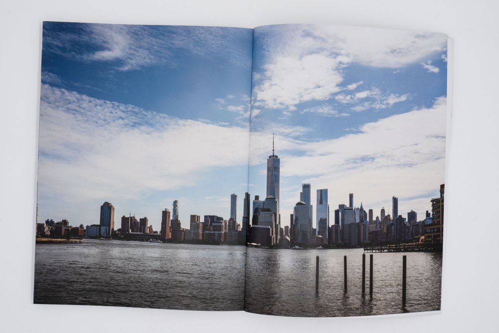 Panoramic view of Manhattan skyline across water under bright blue sky with white clouds.