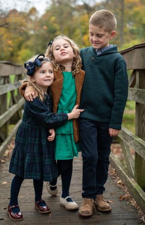 Three children posing together on a wooden bridge during autumn.