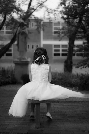 Young dancer in white dress sitting on bench viewed from behind.