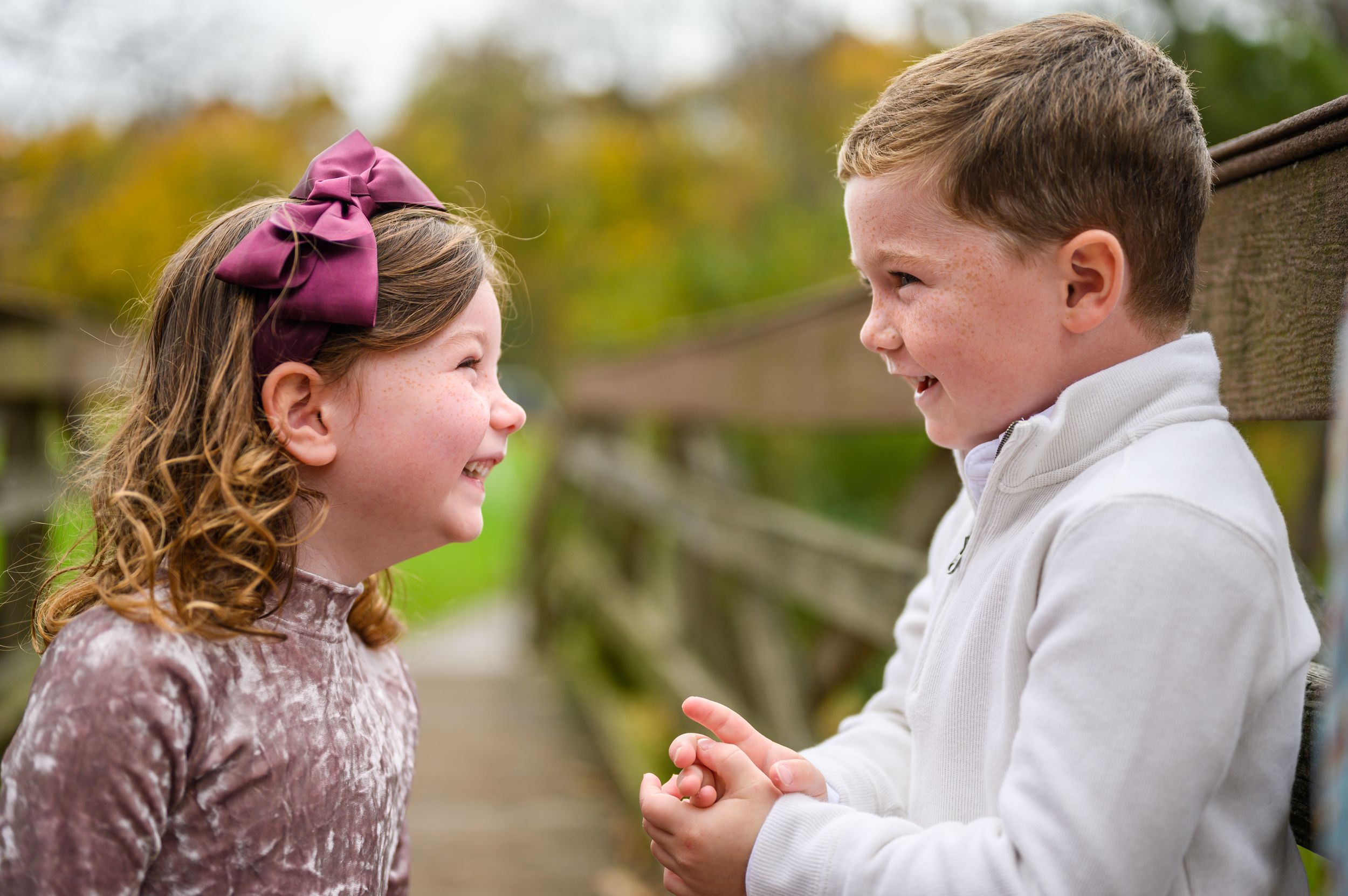 Two children sharing a playful moment on a wooden bridge.