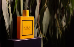 Orange Gucci perfume bottle displayed against eucalyptus leaves in dramatic lighting.