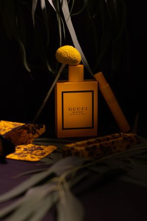 Gucci fragrance bottle with dried flowers and decorative elements in moody dark lighting.