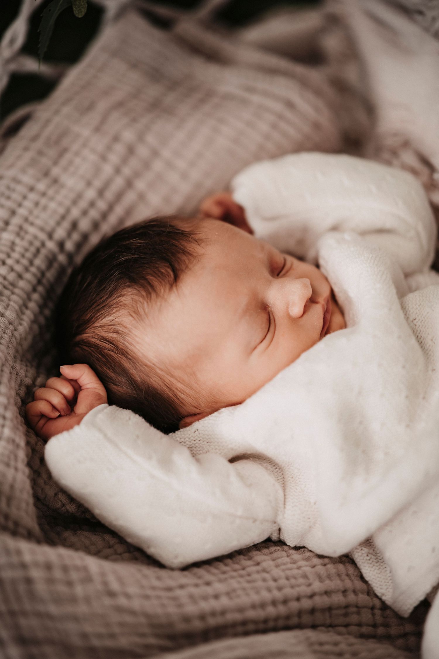 A sleeping infant in white clothing rests peacefully on brown quilted bedding.