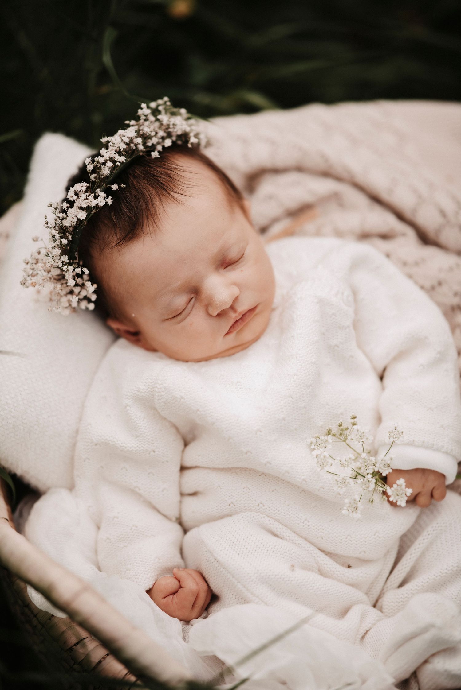 A sleeping newborn wears a delicate crown of baby's breath flowers against white bedding.