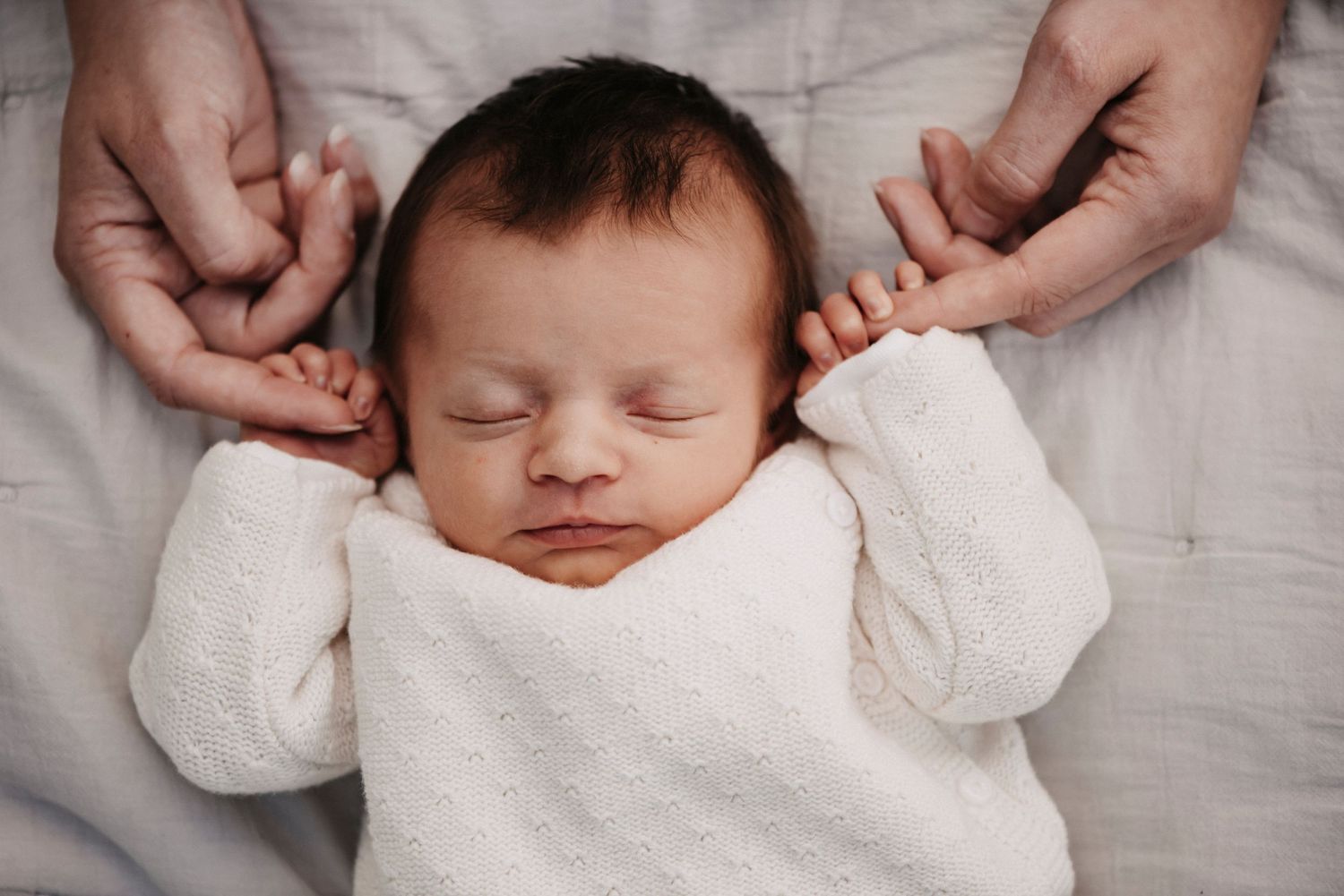 A sleeping newborn in white clothing rests peacefully on soft fabric.