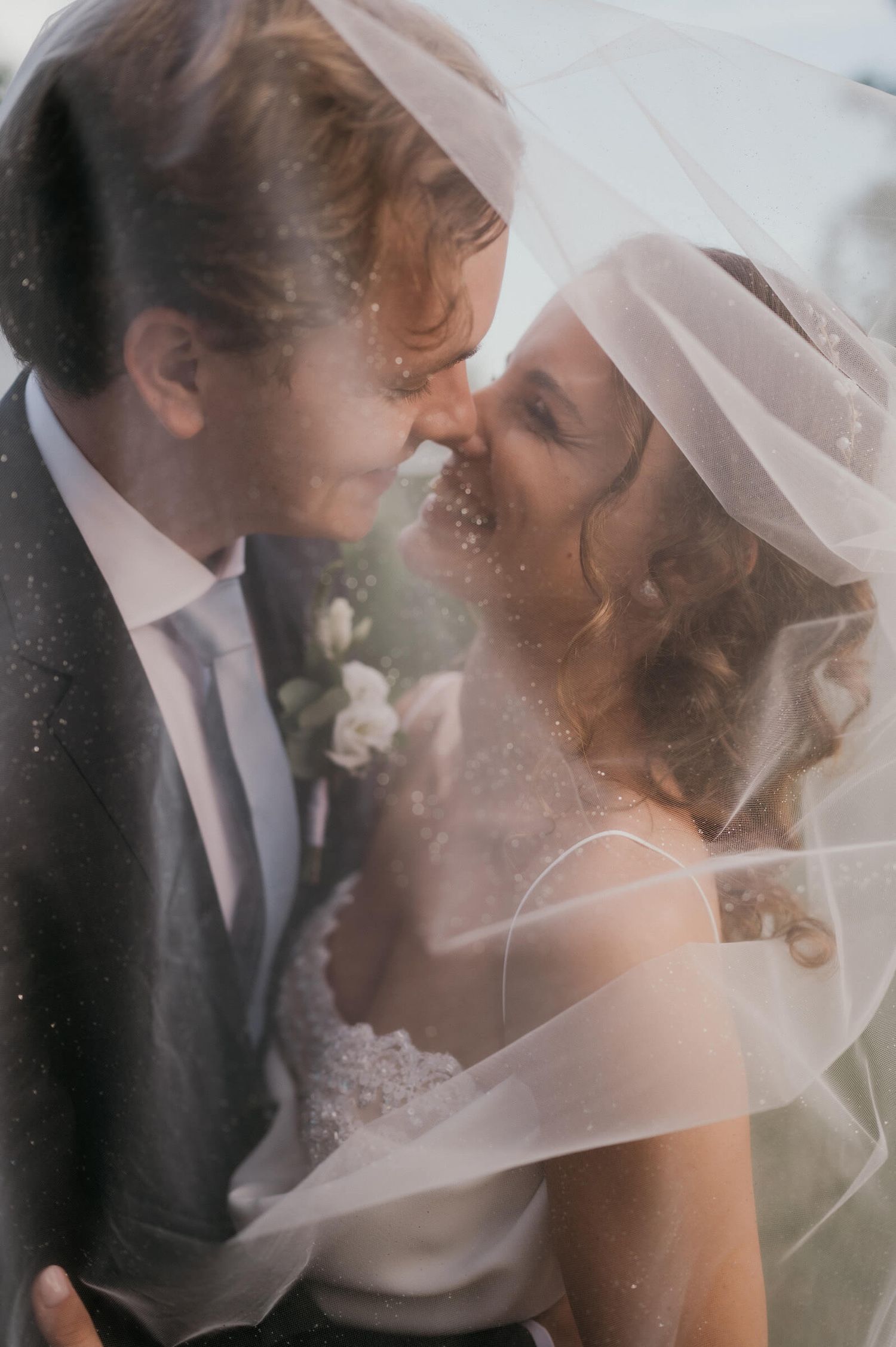 Romantic close-up of newlyweds embracing under a delicate veil.