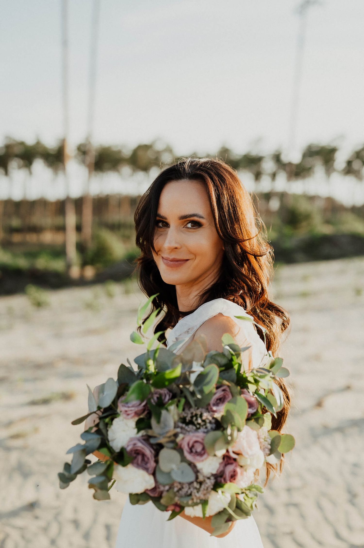 Woman holding an elegant bouquet of pink roses and greenery in outdoor setting.