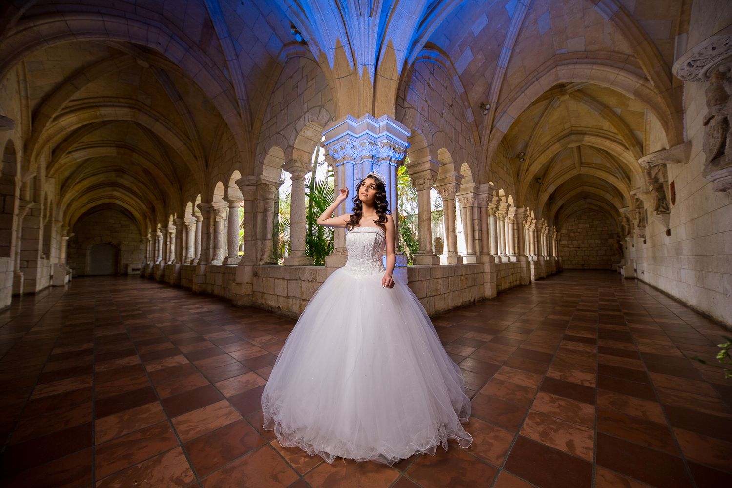 Wedding gown flowing in a gothic vaulted monastery hallway with dramatic lighting.