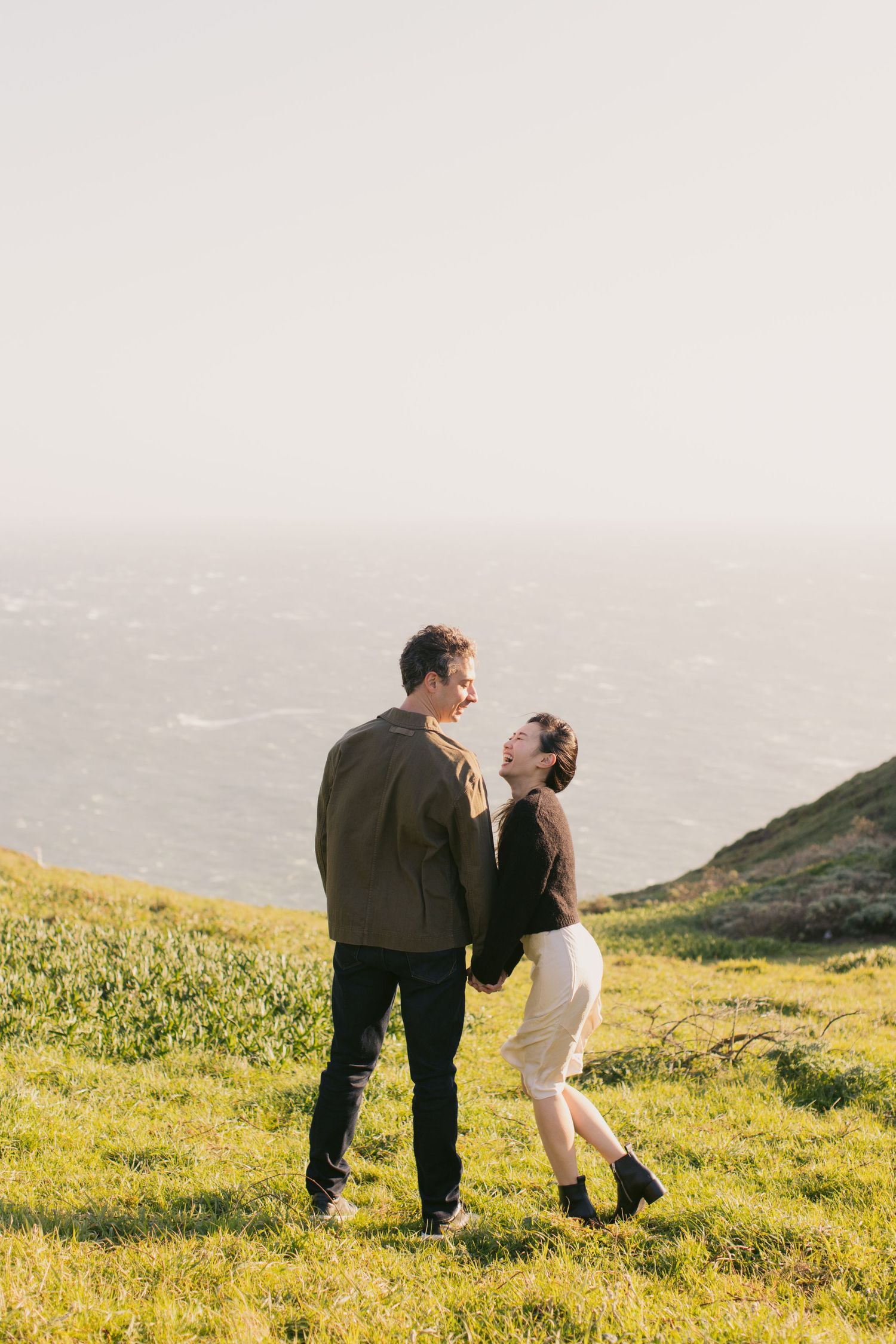 Joyful couple enjoying a romantic moment on a coastal hillside during golden hour.