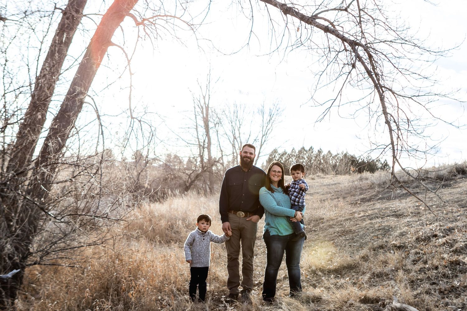 A family enjoying a winter walk together through barren trees on a hillside trail.