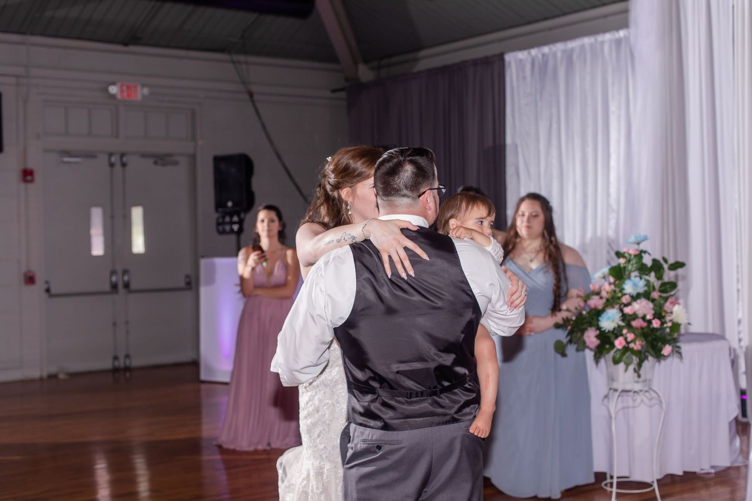 Groomsmen in gray suits share a lighthearted moment during wedding photos against white drapes.