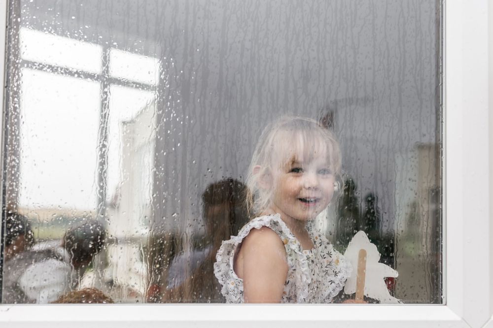 Child with bright eyes presses against window glass with joyful expression.