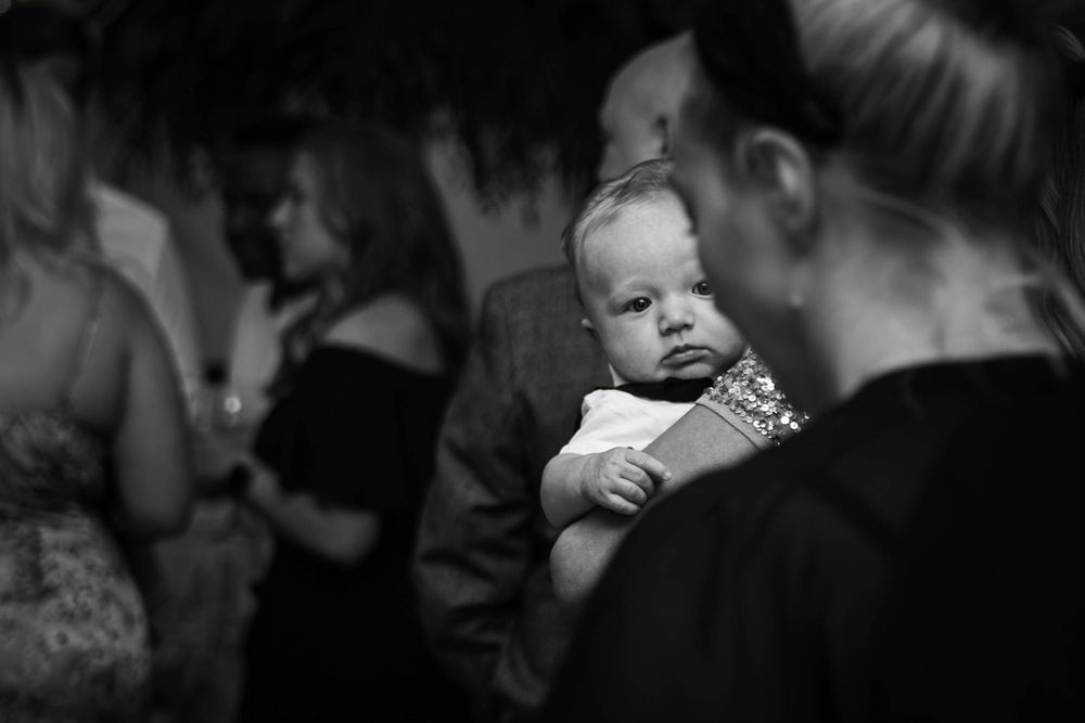 A small baby peeks over someone's shoulder during a social gathering.