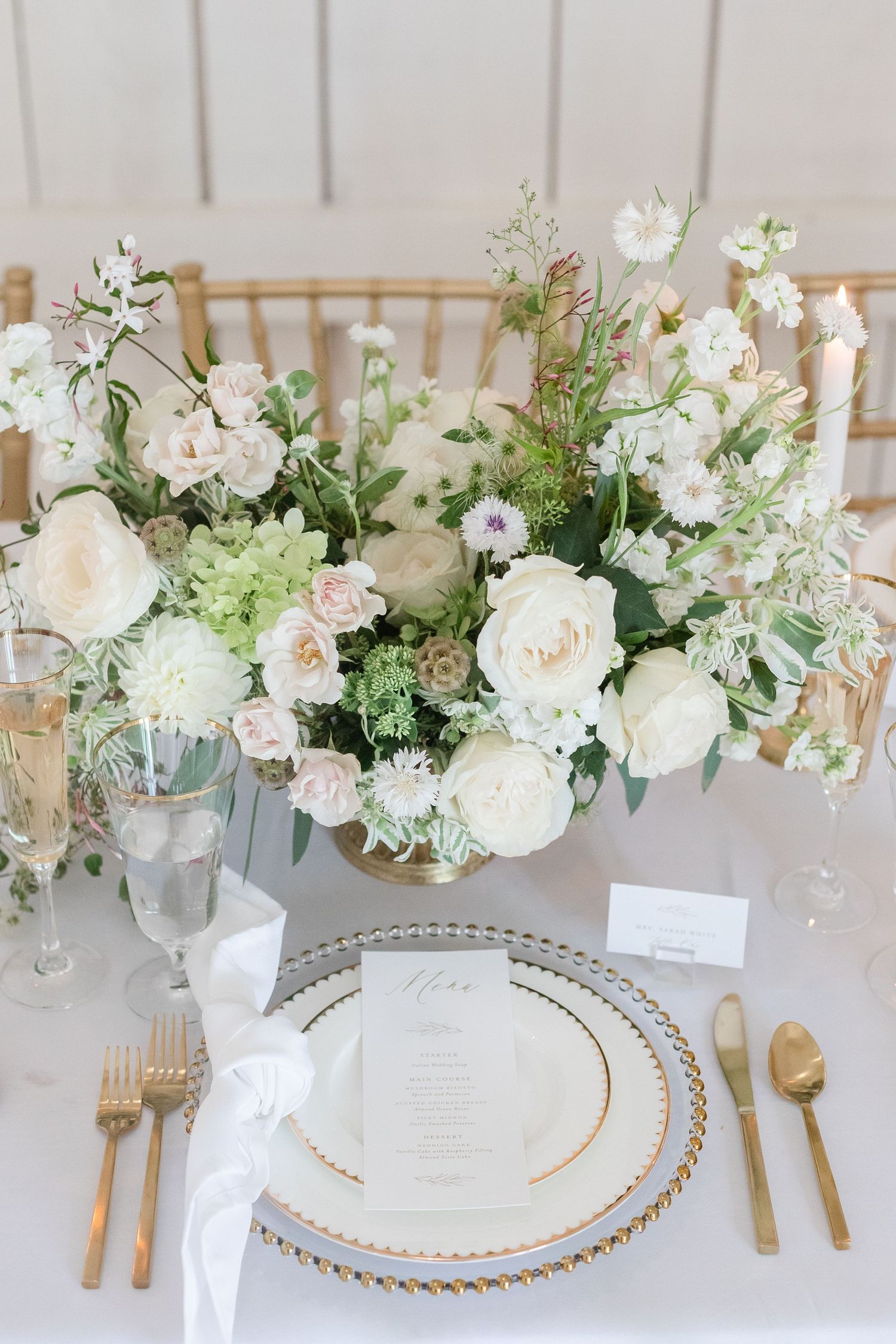 Elegant white table setting with floral centerpieces and gold accents at a wedding reception.
