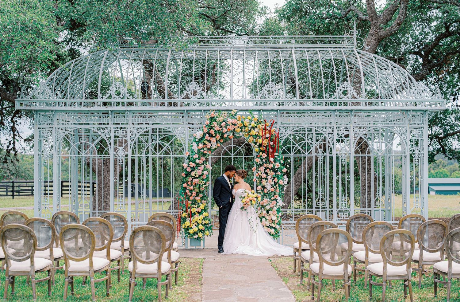 A romantic greenhouse wedding ceremony setup with white chairs and floral arch decorations surrounded by lush greenery.