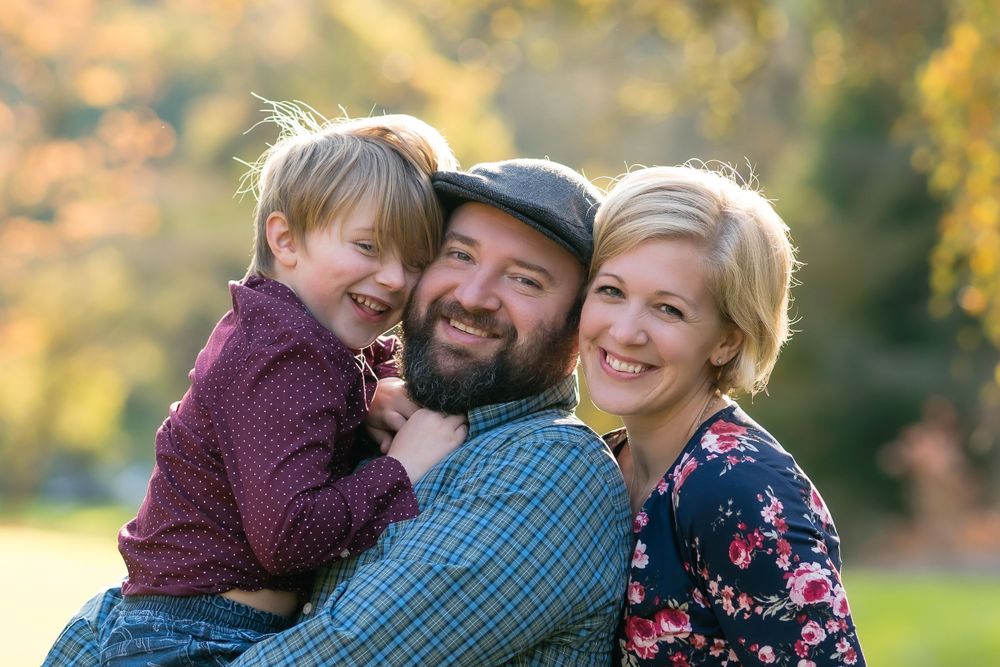 A joyful family portrait taken outdoors with warm autumn colors in the background.