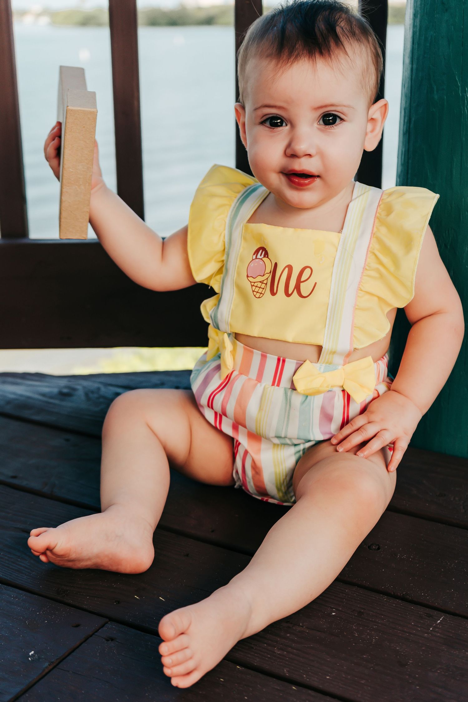 Outdoor Cake Smash Session at Maximo Park in St. Pete, FL; baby holding wooden toy and smiling