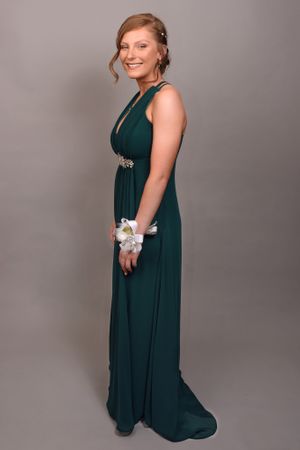 Woman in a dark teal formal dress posing against a grey studio backdrop.
