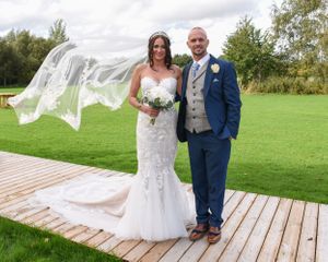 Wedding couple poses on wooden walkway in outdoor garden setting.