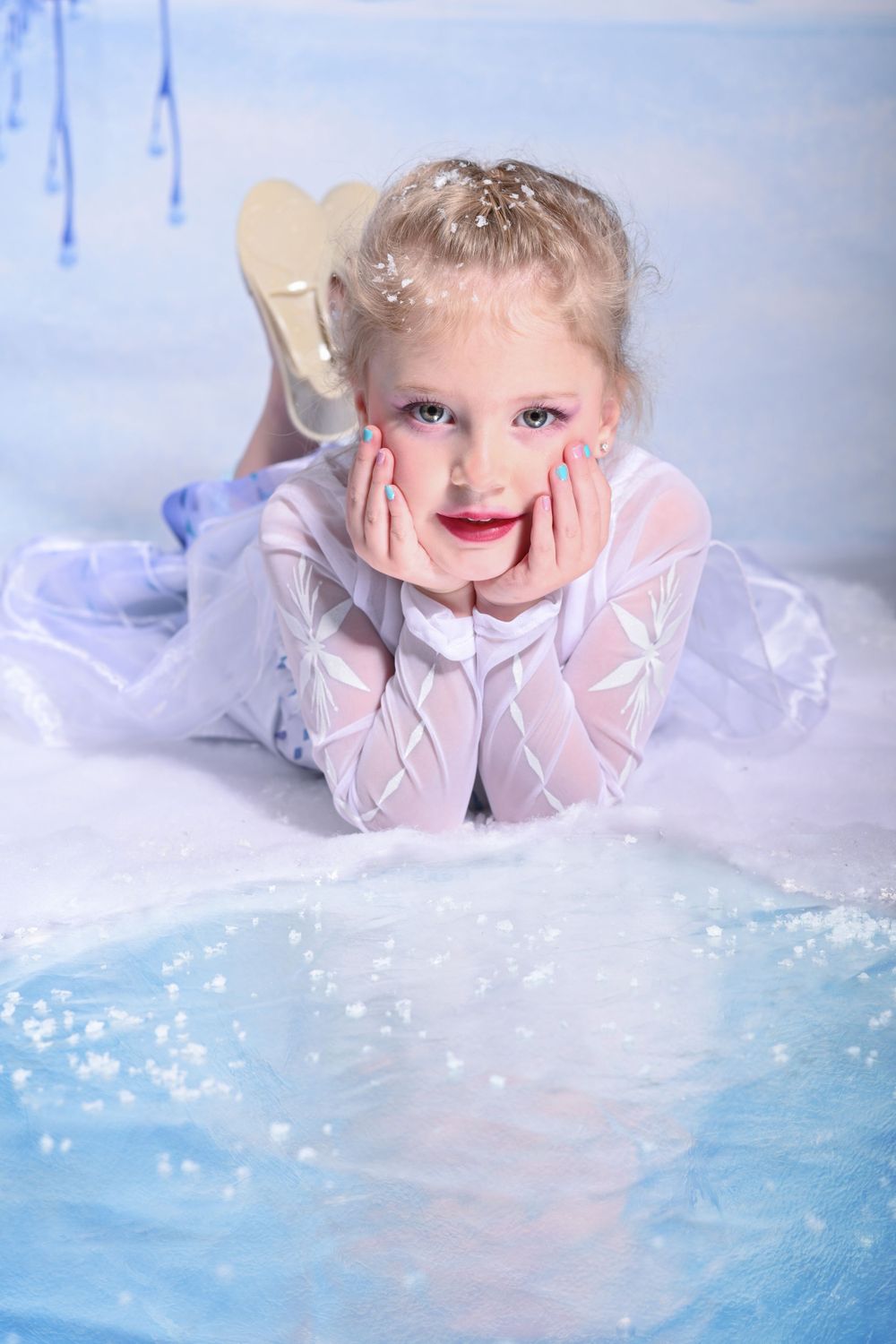 A child in a white dress poses on a sparkly blue backdrop with magical effects.