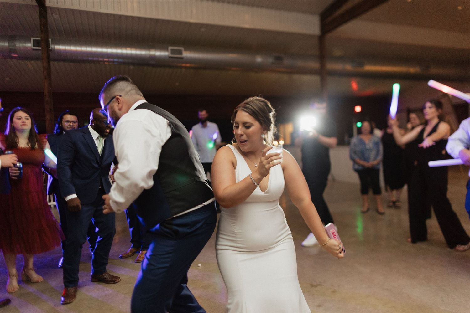 Wedding guests dancing energetically under colorful lights at an indoor reception venue.