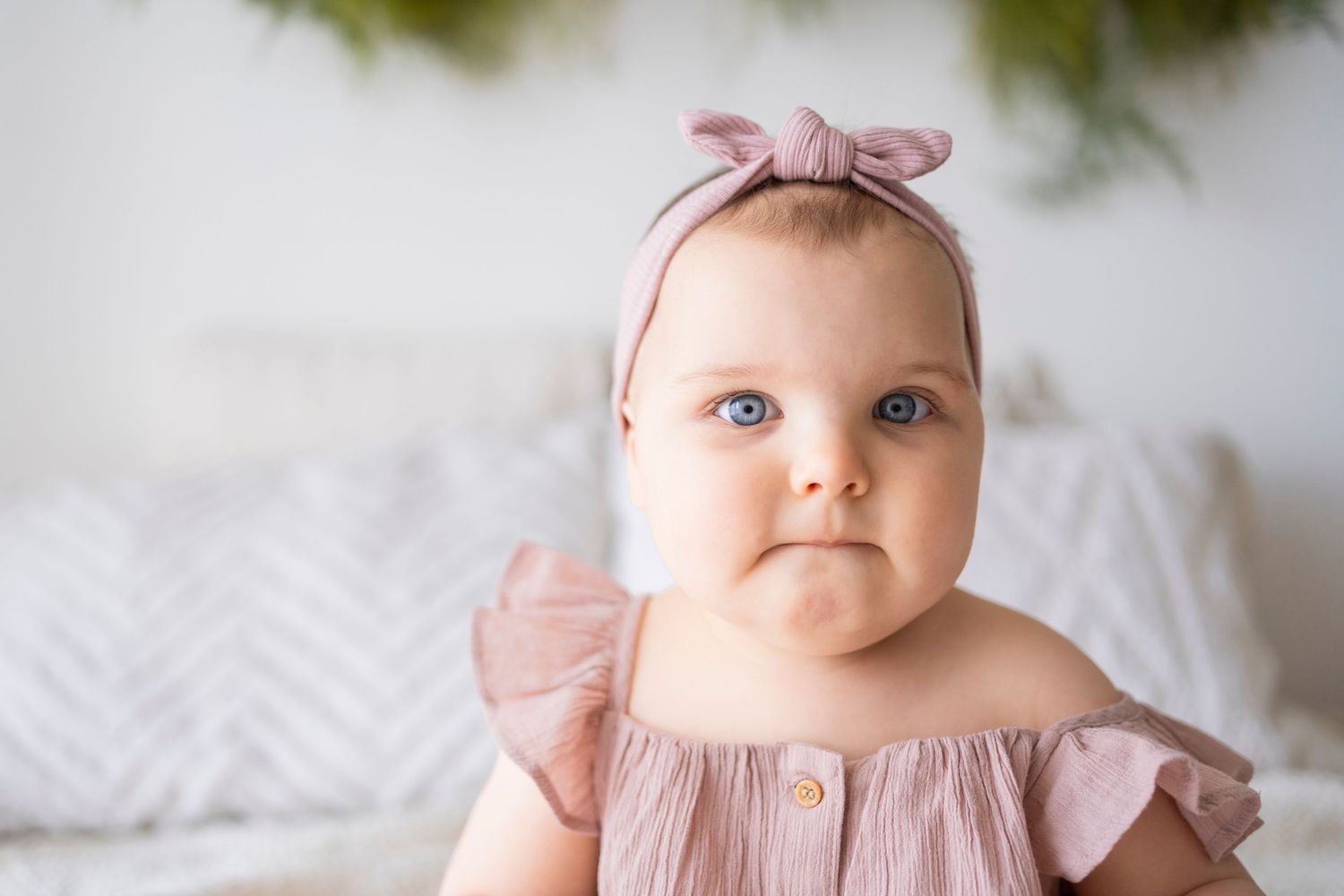 Close-up portrait of blue-eyed baby girl wearing pink bow headband and ruffle dress.