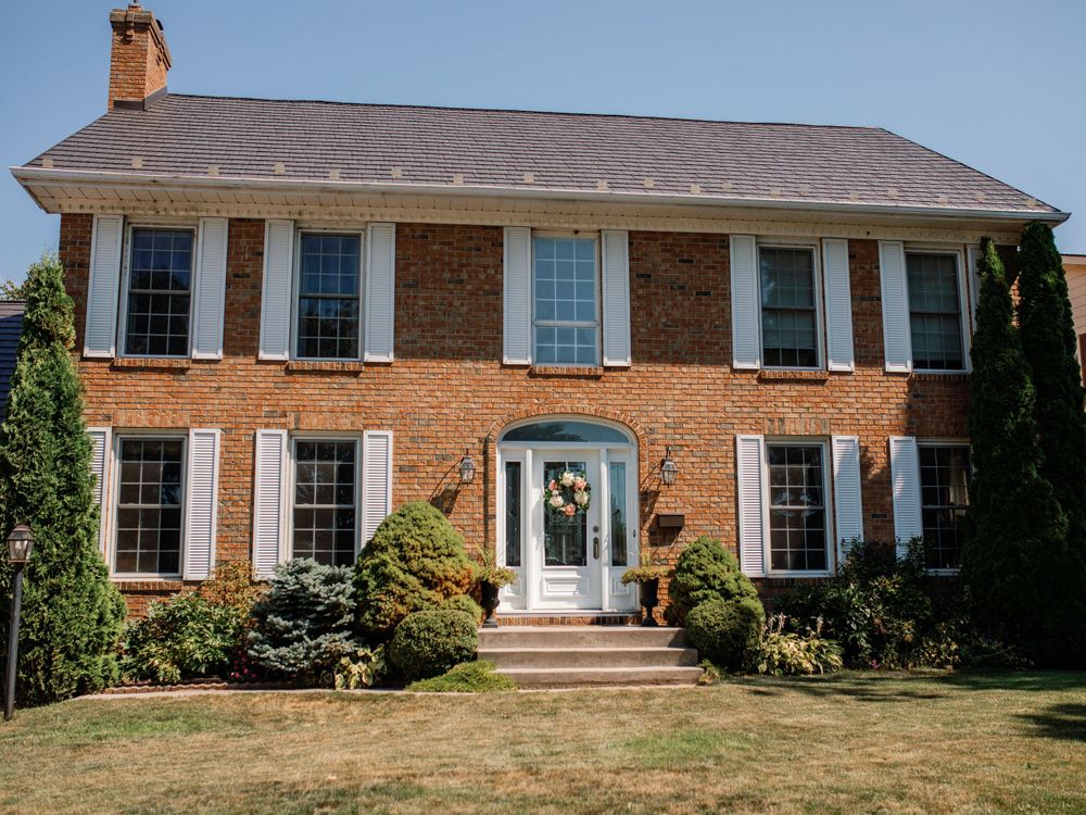 Exterior view of a large brick colonial style house with white trim and multiple windows.