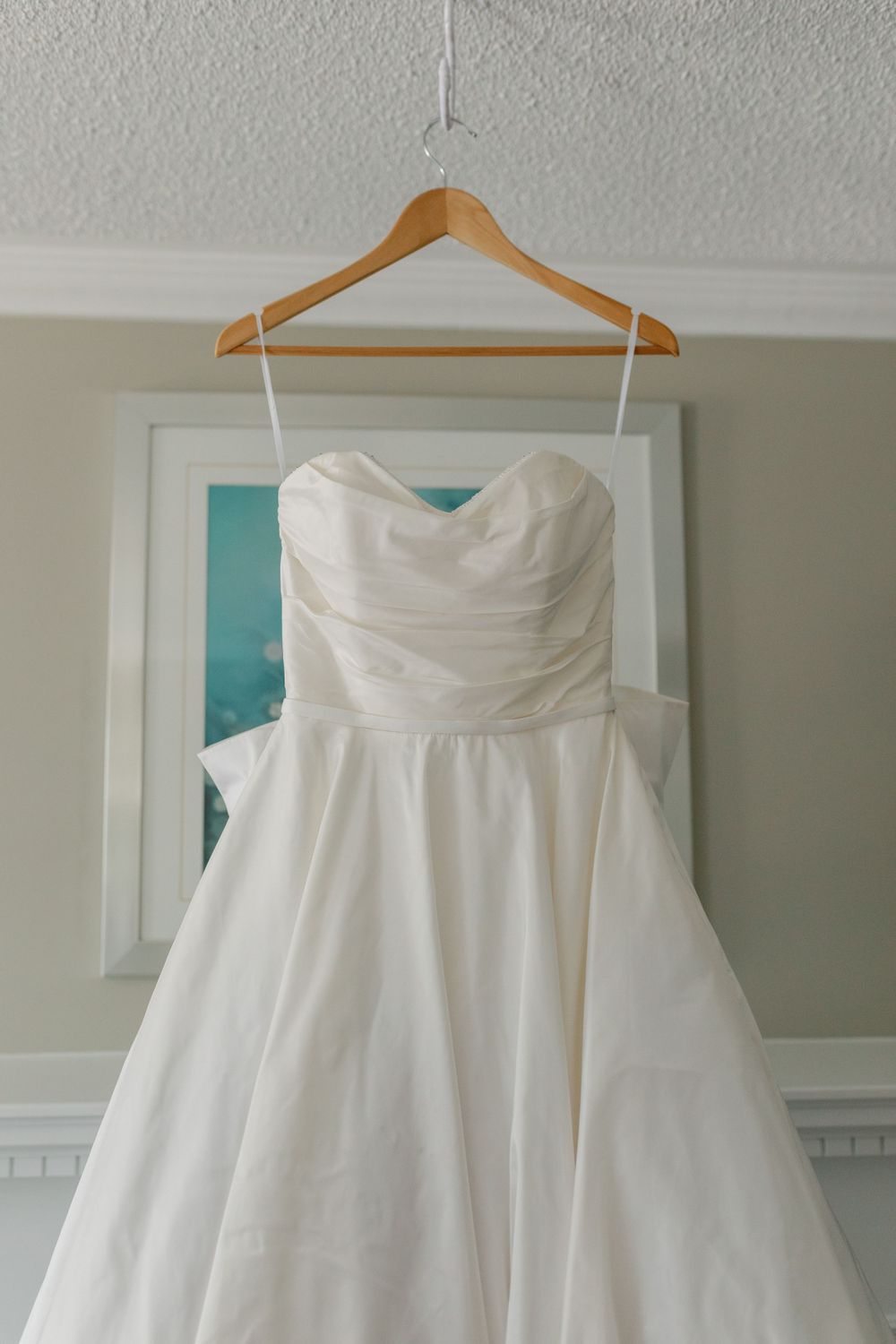 Close-up details of an elegant strapless white wedding gown on a wooden hanger.