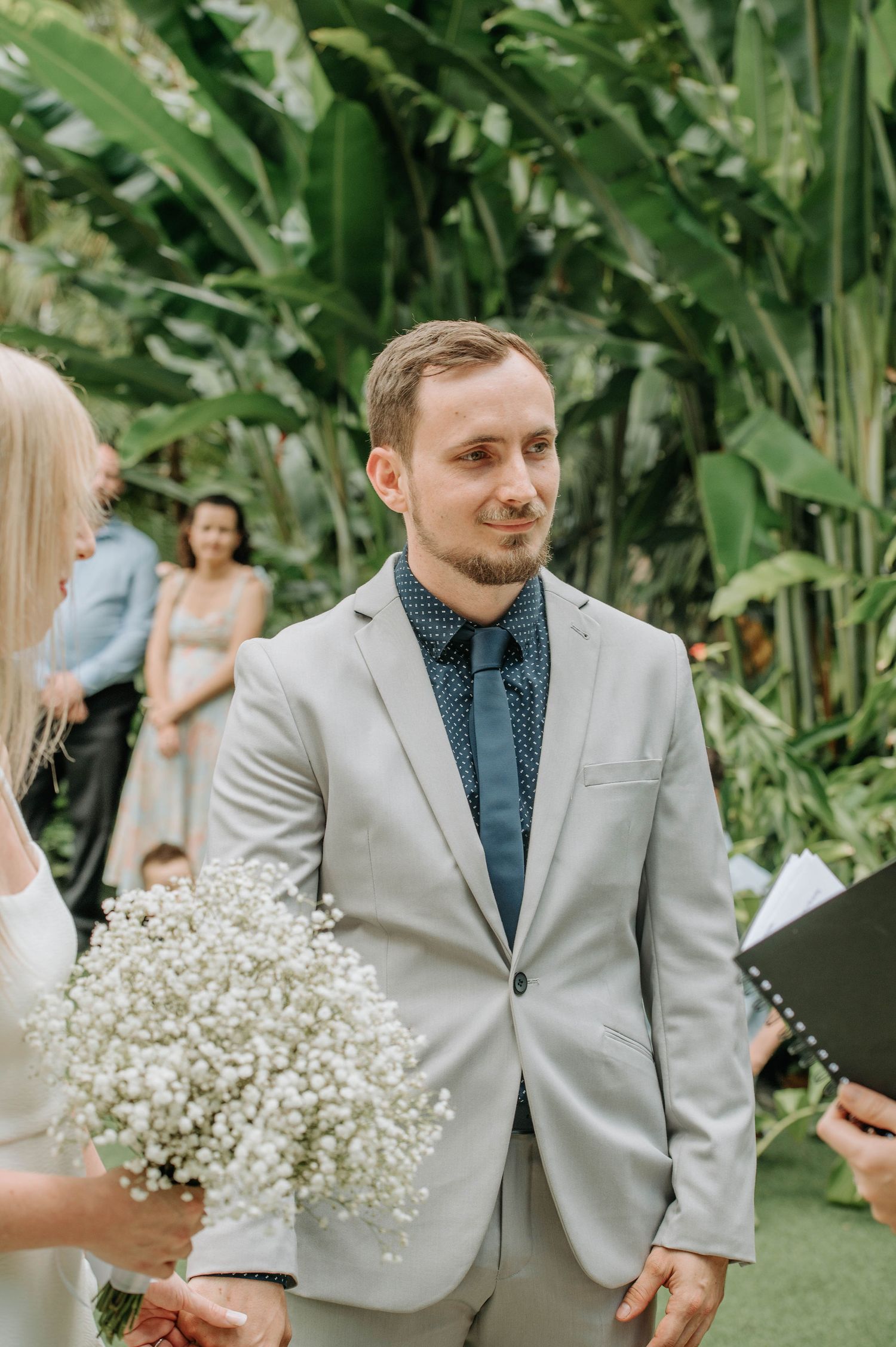 Wedding ceremony in a tropical garden setting with guests and blooming flowers.