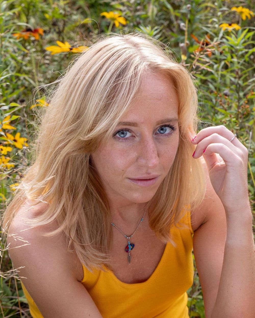 Portrait of a woman in a yellow top posing against a garden background with orange flowers.