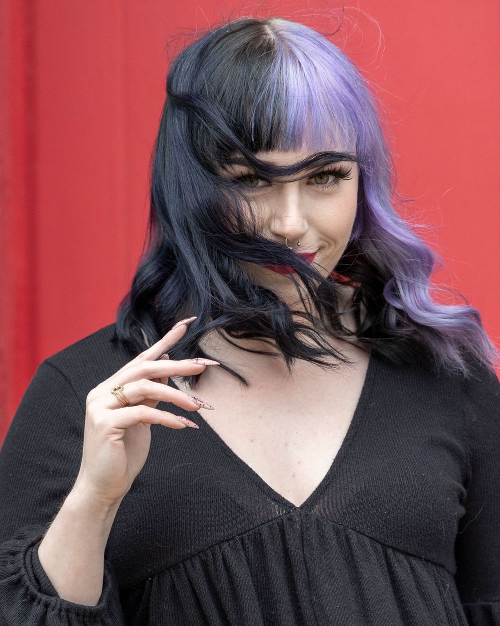 Dramatic portrait with purple-tinted hair and black top against vibrant red background.