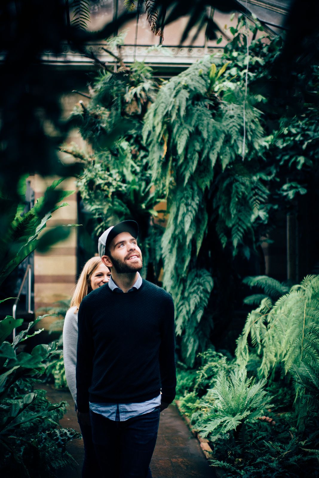 Couple standing among lush tropical plants in an indoor garden setting.