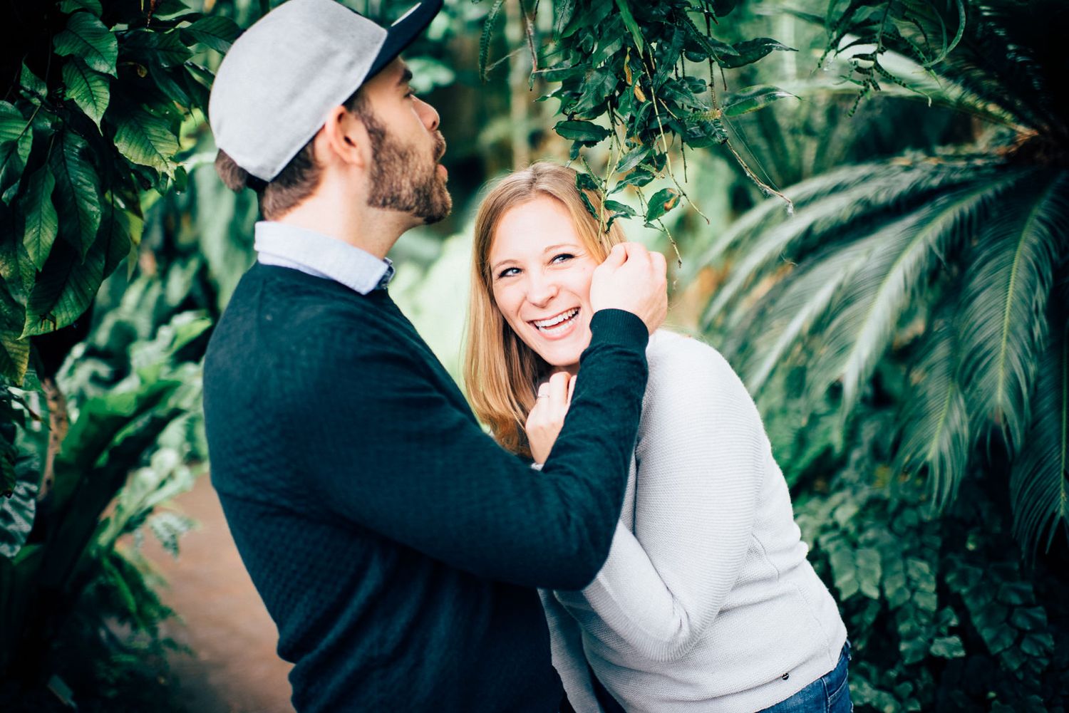Sweet interaction between couple surrounded by tropical plants in a greenhouse setting.