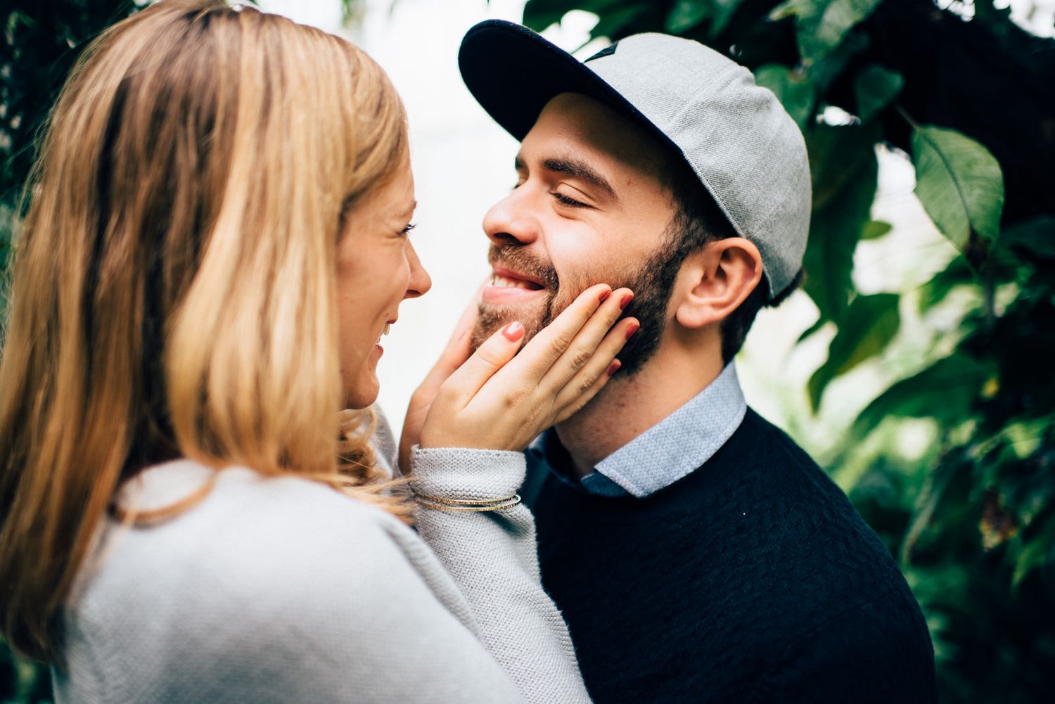 Intimate moment captured between couple in casual wear against a backdrop of green foliage.