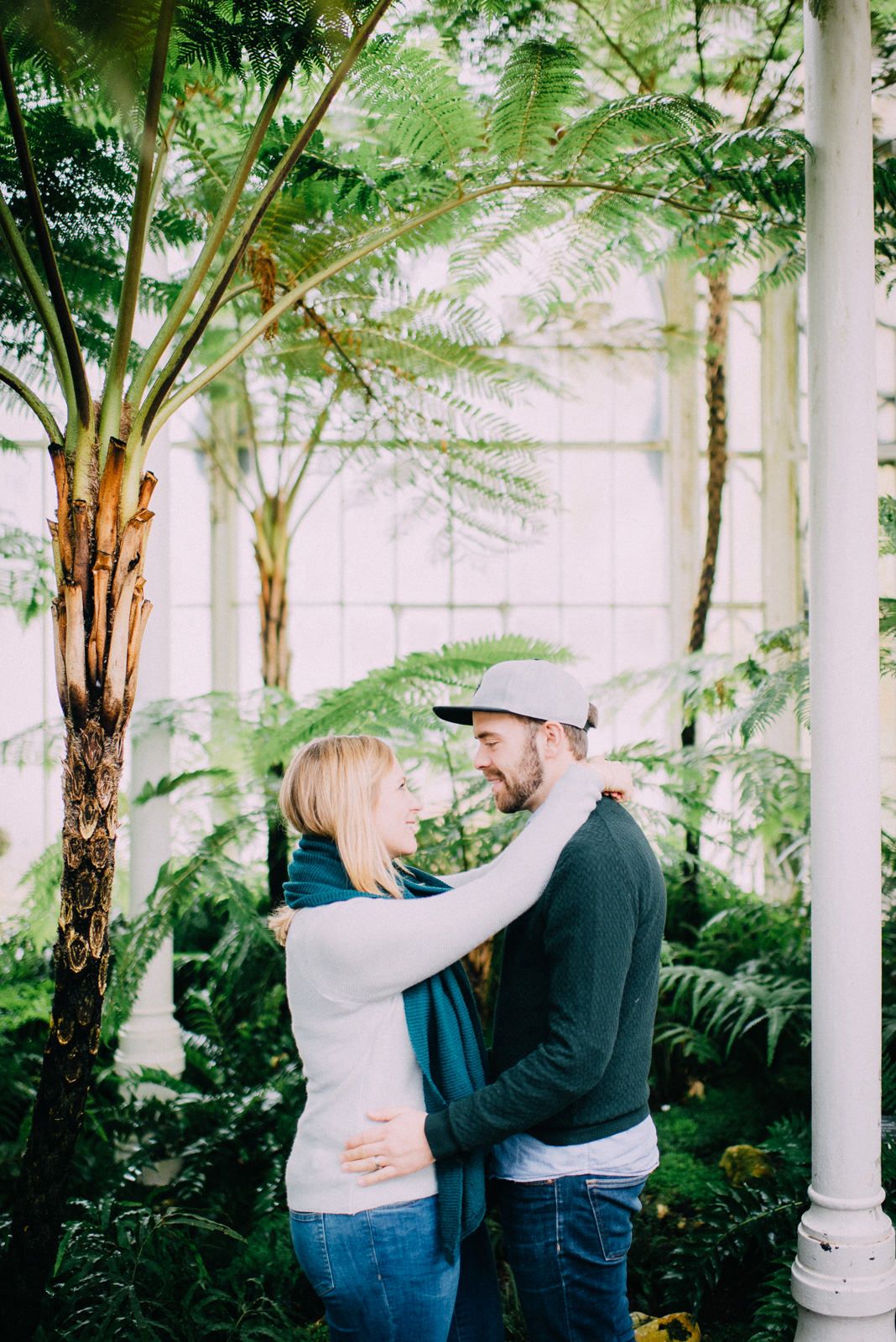 Tender embrace captured in a lush greenhouse setting with ferns and tropical plants.