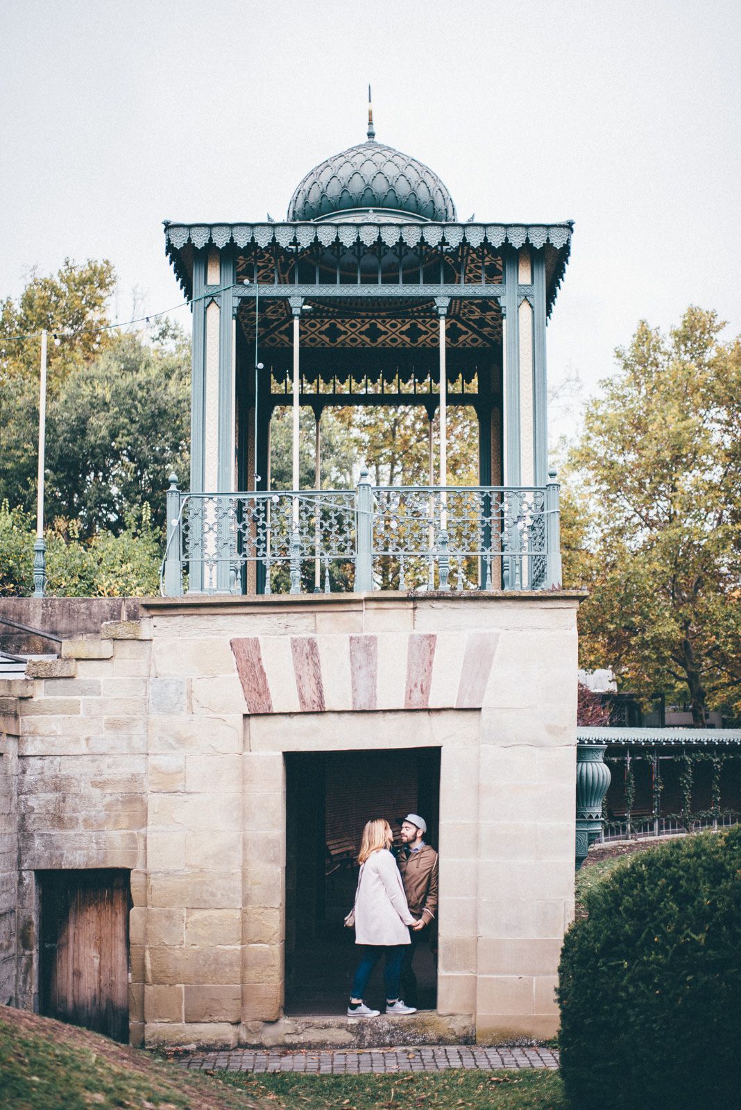 Ornate blue and white Victorian gazebo with couple standing in stone archway below.