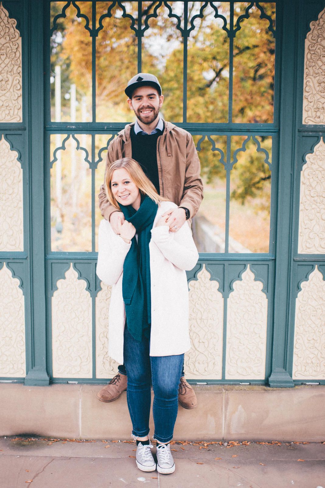 Couple posing in front of decorative gothic-style window with ornate architectural details.