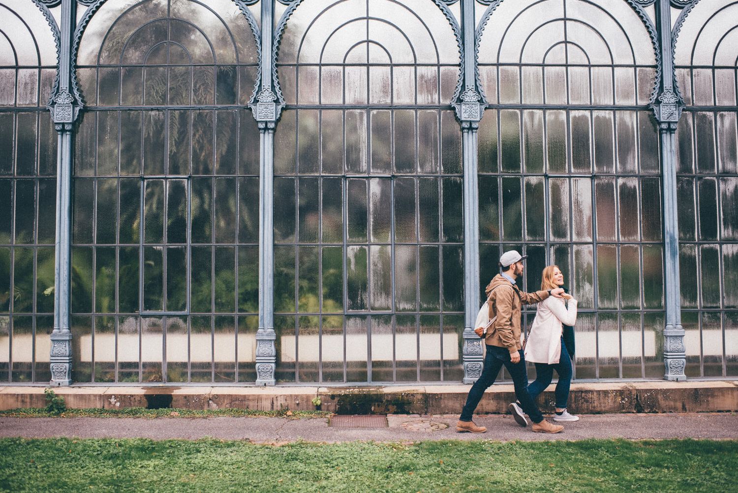 A couple walks past architectural arches and iron railings on a path outside a historic building.