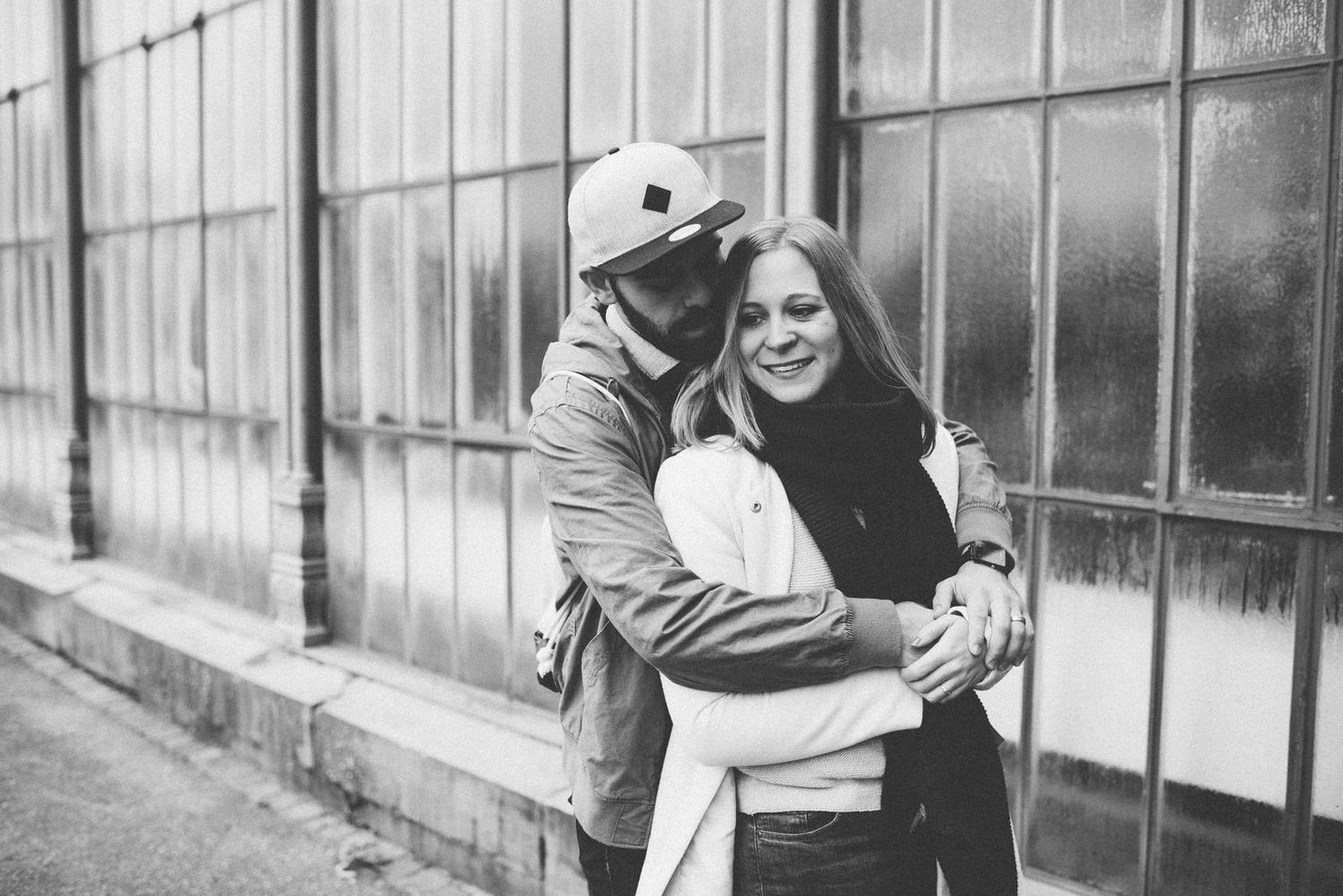 A romantic black and white moment of a couple embracing against a building exterior.