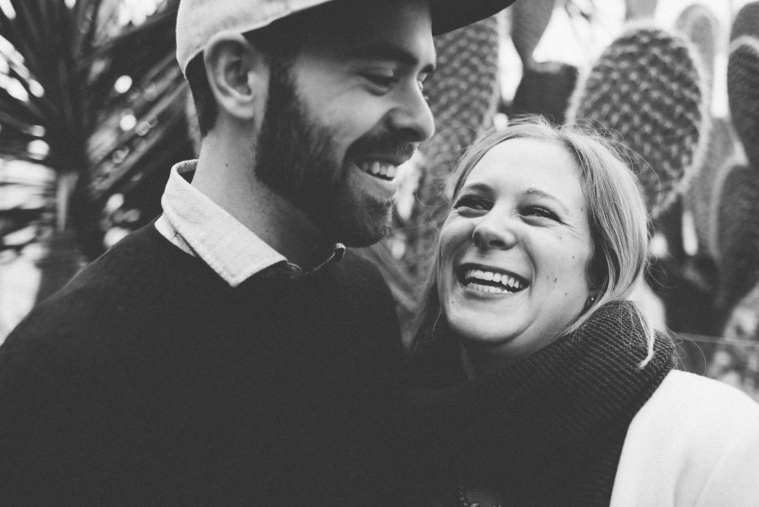 Black and white portrait of laughing couple with cactus garden background.