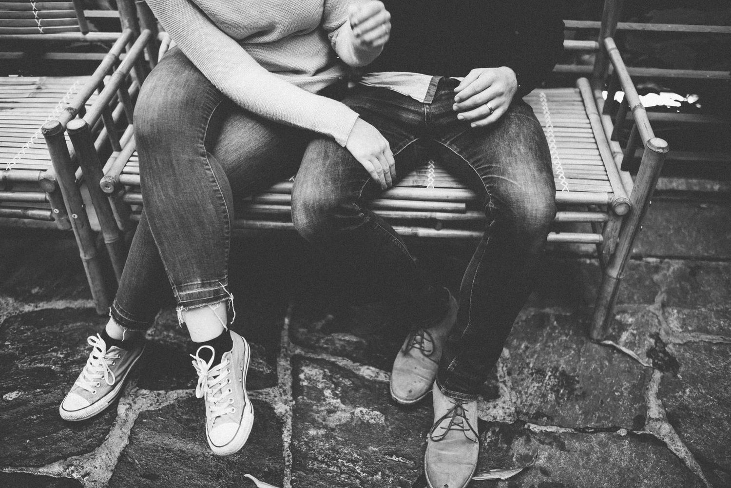 Close-up view of a couple's legs sitting on a wooden bench wearing contrasting casual footwear.