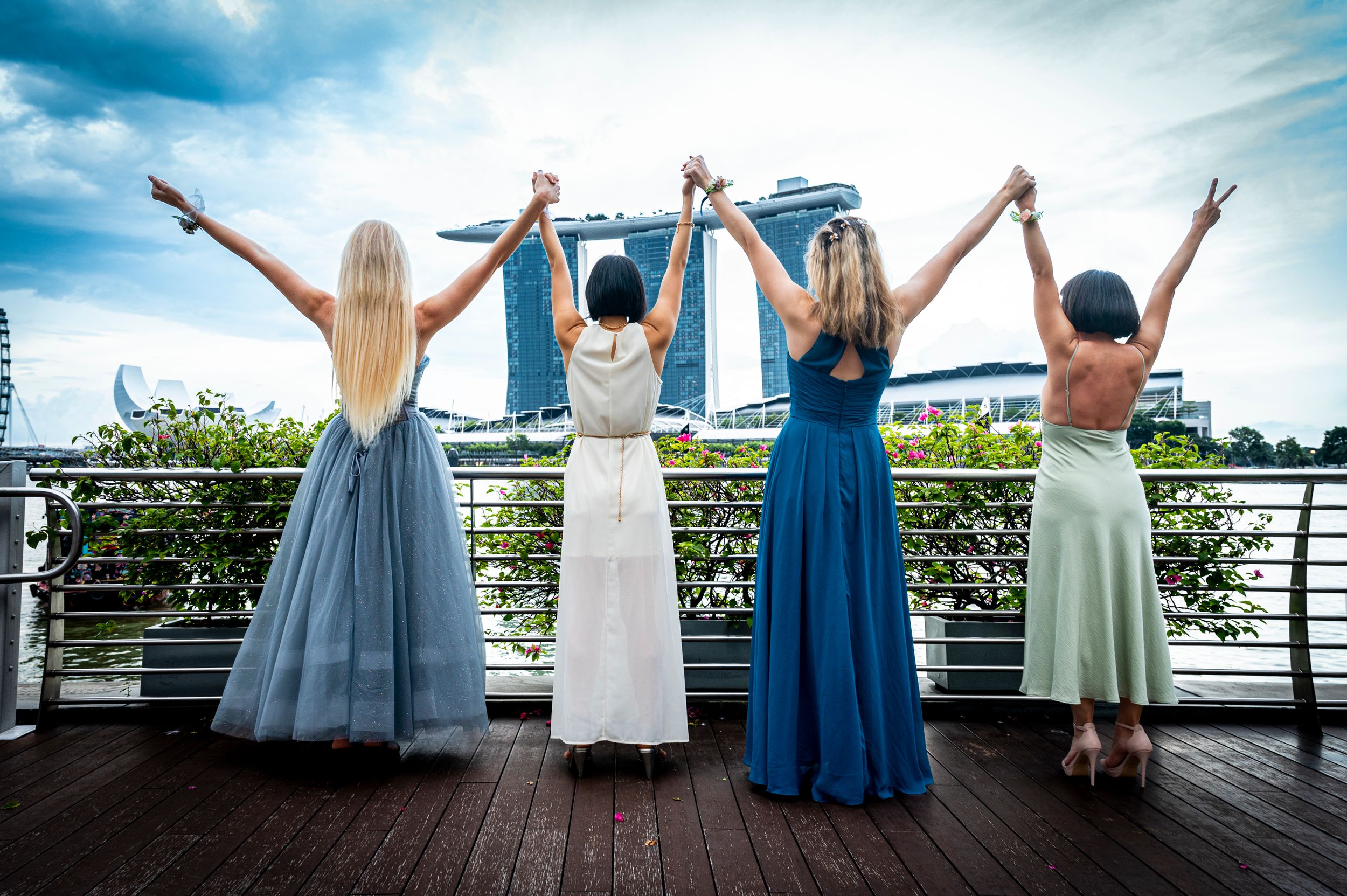 Four people in flowing dresses raise their arms against Singapore skyline at Marina Bay Sands. Scotch Plains Photographer, portrait photo