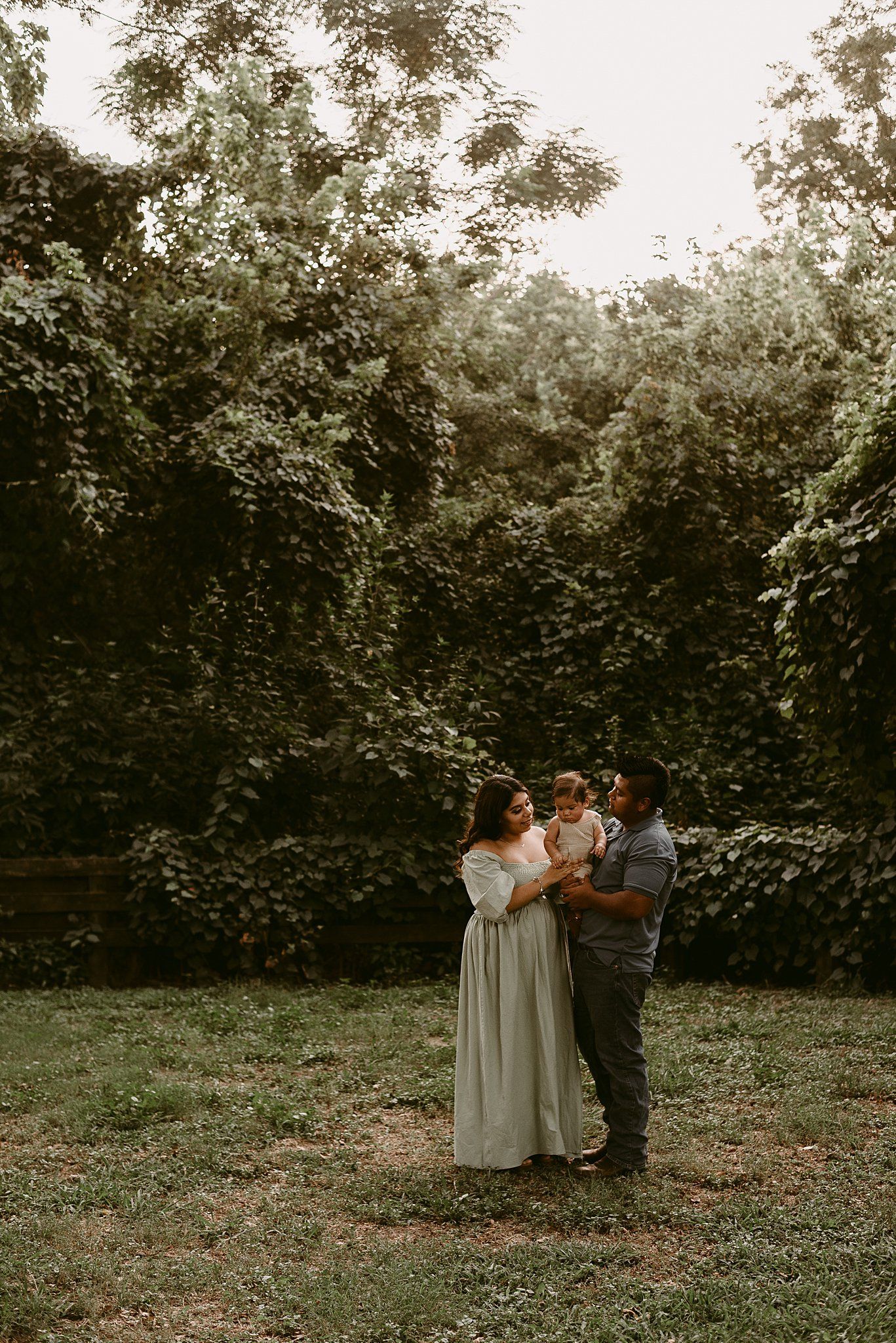 Family portrait session against green foliage wall during golden hour.