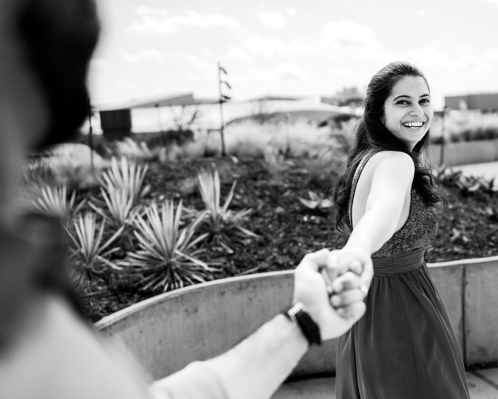 A black and white engagement photo showing a couple holding hands in an outdoor garden setting.