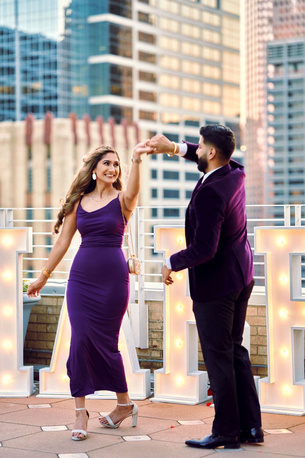 Couple dancing on rooftop terrace with city skyline backdrop at sunset.