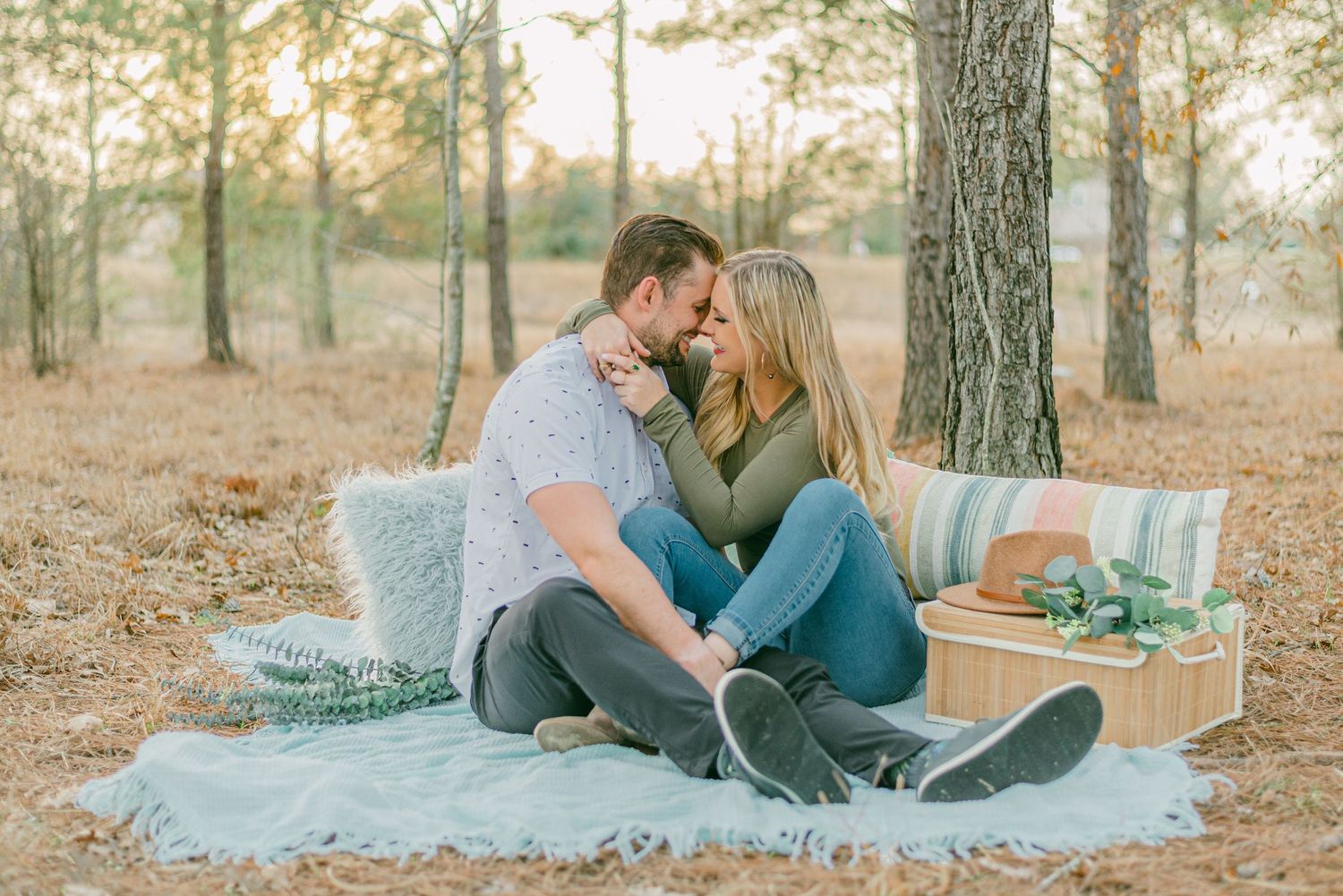 a couple wrapped in each other's arms go in for a kiss on a picnic blanket in the woods
